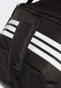 Bolsa de lona negra con rayas blancas, correa ajustable, superficie texturizada y bolsillo exterior para mayor almacenamiento y accesibilidad.