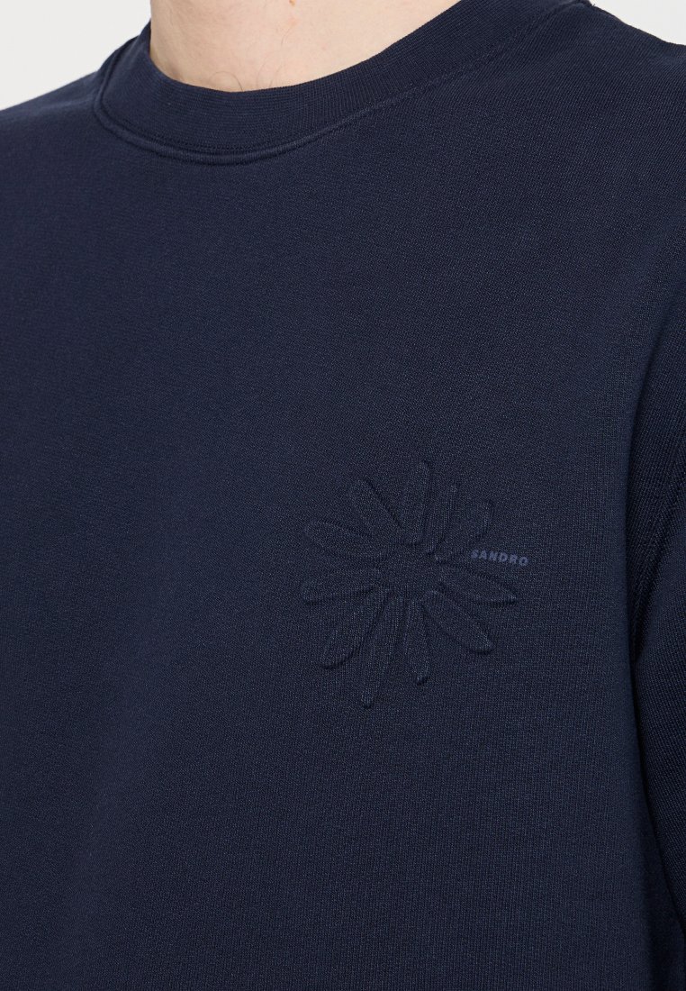 Navyblauwe sweatshirt met een ronde hals en een textuurpatroon van bloemen op de linkerkant van de borst. Materiaal lijkt zacht en iets dik.
