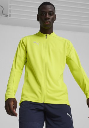 Puma zip-up jack in felgeel, gemaakt van gladde stof, met lange mouwen en een klein logo op de borst.