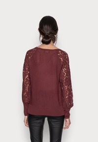 Bordeauxfarbener Pullover mit langen Spitzenärmeln, Rundhalsausschnitt und elastischen Bündchen. Figurbetonter Schnitt mit strukturiertem Strick und floralen Spitzelementen.