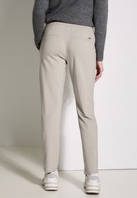 Beiga skräddarsydda byxor i ett slätt tyg, med bakfickor och slim fit; tillsammans med ljusa sneakers mot en neutral bakgrund.