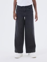 Jeans de denim negro de pierna ancha con una cintura alta, cinco bolsillos y dobladillos enrollados, combinados con zapatillas blancas sobre un fondo neutro.