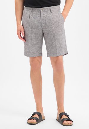 Man wears gray textured knee-length shorts with side pockets, a black shirt, and black buckle sandals, standing with hands relaxed.