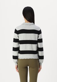 Harmaa neule mustilla raidoilla, kauluksellinen kaula, pitsikuvioiset hihansuut ja helma. Yhdistetty oliivinvihreisiin legginsseihin.