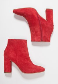 Bottines en daim rouge avec un bout pointu, une fermeture éclair latérale et un talon épais pour plus de stabilité. Texture lisse sur toute la surface.