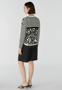 Zwart-wit gestreepte trui met abstracte patronen, ronde halslijn en lange mouwen, gecombineerd met zwarte shorts en hoge sandalen.
