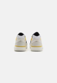 Herrskor i sneakersstil med ett grått och svart ovandel med gula accenter, vit sula, rundad tå och texturerat mönster bakpå.