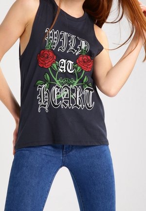 Mouwloos zwart topje met de tekst "WILD AT HEART" en rode roosafbeeldingen, gedragen met een blauwe spijkerbroek, persoon houdt lang rood haar vast.