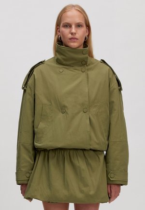 Olivgrüne Jacke mit hohem Kragen und doppelter Knopfleiste. Hat voluminöse Ärmel und eine geraffte Taille. Bedruckter Stoff.