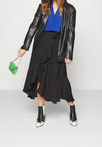 Gonna midi nera a balze abbinata a una camicia azzurra a bottoni, una giacca di pelle nera e stivaletti neri con accenti bianchi. Piccola borsa verde.