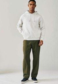 Sudadera gris claro con textura en relieve, capucha con cordones, bolsillo tipo canguro en la parte frontal; combinada con pantalones rectos de color verde oliva y zapatillas de deporte azul marino.
