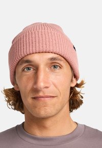 Beanie a coste rosa con risvolto, indossata da una persona con capelli di lunghezza media, abbinato a una maglietta grigia. Branding minimal visibile.