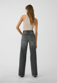 Jeans z visokim pasom in širokimi hlačnicami v temno sivi denim tkanini s svetlim obarvanjem. Imajo velike zadnje žepe in surov rob.