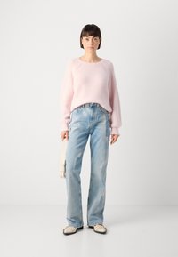 Light pink knitted sweater with dropped shoulders, paired with light blue high-waisted jeans featuring patchwork. Model holds a light bag.