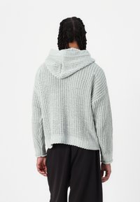 Sudadera de punto verde claro con un patrón texturizado, mangas anchas y un diseño corto. Presenta una capucha grande y un dobladillo acanalado.