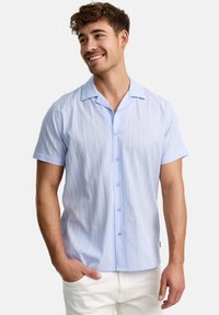 Lichtblauwe shirt met korte mouwen en verticale strepen, met knoopsluiting en een puntige kraag, gedragen met witte broek. Gladde stoftextuur.