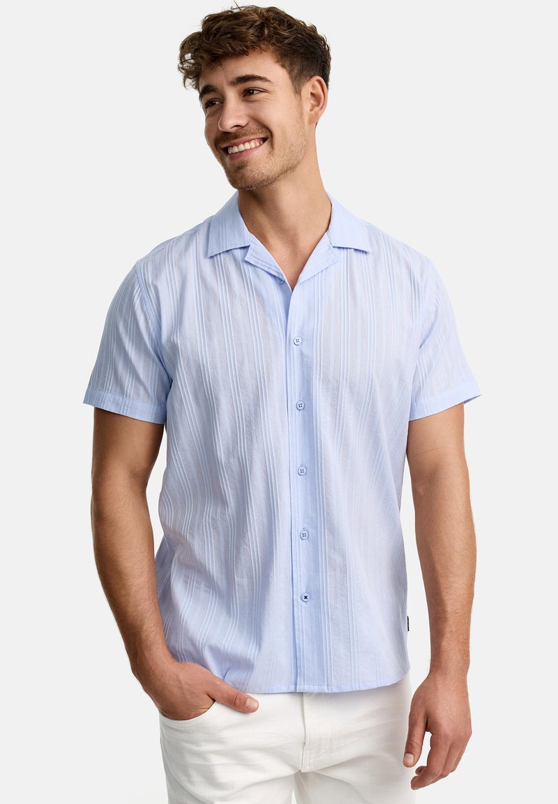 Lichtblauwe shirt met korte mouwen en verticale strepen, met knoopsluiting en een puntige kraag, gedragen met witte broek. Gladde stoftextuur.