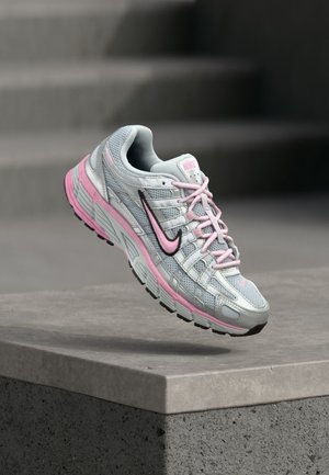 Grå og lyserød Nike løbesko med mesh-overdel og polstret sål, placeret i luften over en grå betonforkant og trin.
