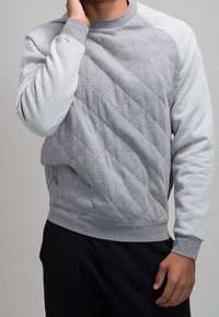 Szara bluza wykonana z teksturowanej tkaniny, z wykrojem w romby na przodzie i jednolitymi szarymi rękawami. Okrągły dekolt i ściągacze przy rękawach.