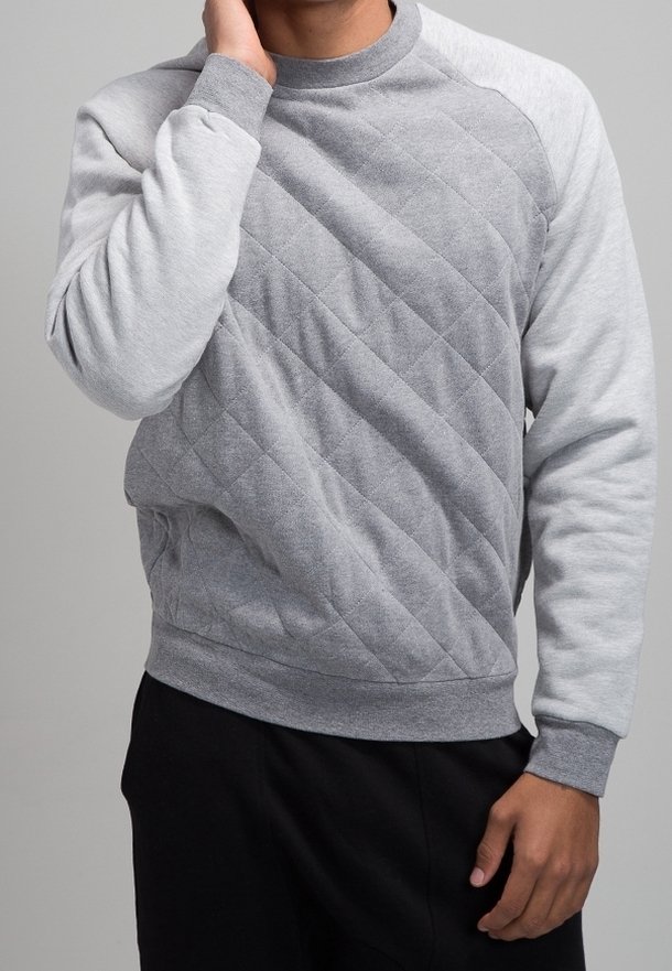 Szara bluza wykonana z teksturowanej tkaniny, z wykrojem w romby na przodzie i jednolitymi szarymi rękawami. Okrągły dekolt i ściągacze przy rękawach.