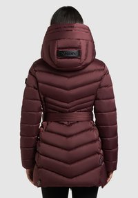 Vijolična puhovka z vzorcem cik-cak šivov, pasom z zaponko in veliko kapuco z logotipno nalepko na hrbtni strani. Gladek, sijoč zaključek.