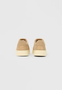 Ζευγάρι μπεζ σουέντ αθλητικών παπουτσιών με κρέμα σόλες από καουτσούκ, που φαίνονται από πίσω, με ετικέτες λογοτύπου GANT στις φτέρνες.