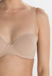 Beige stroppeløs bh med en glatt, formet design, som har mykt stoff, undertrådstøtte og klare justerbare stropper for en diskret look.