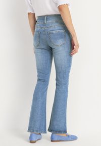 Vaaleansinisiä korkeavyötäröisiä leveälahkeisia farkkuja, joissa on kaksi takataskua ja klassinen farkkukangas, yhdistettynä sinisiin tasapohjakenkiin.