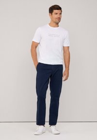 Witte t-shirt met korte mouwen en zwarte tekst, gecombineerd met marineblauwe broek en witte sneakers. Eenvoudig en aansluitend ontwerp.