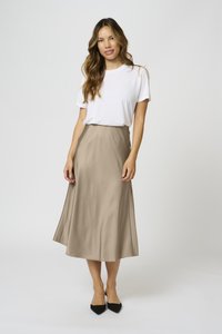 Heledbeez satin midi seelik, millel on sile tekstuur ja voolav siluett, koos valge T-särgi ja mustade terava ninaga kingadega.