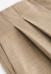 Beige geplooid stof met een gladde textuur en een subtiel geweven patroon, met accent op stikdetails en een lichtgewicht ontwerp.