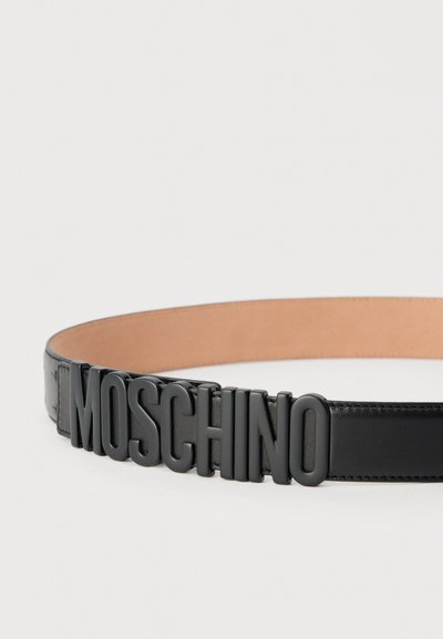 Μαύρη δερμάτινη ζώνη με μεγάλα ανάγλυφα μαύρα γράμματα που σχηματίζουν τη λέξη "MOSCHINO" ως λεπτομέρεια πόρπης σε μπεζ εσωτερική επένδυση.