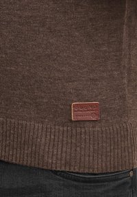Brun strikket sweater med ribbet kant og et lædermærke, der står "BLEND GLOBAL JEANMAKER" med synlig syning.