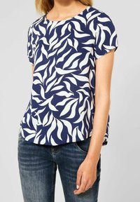 Mörkblå kortärmad topp med vita bladmönster. Rundad halsringning och avslappnad passform. Matchas med blå denimjeans. Slät tygets struktur.