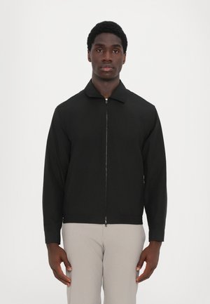 Črna zip-up jakna s ovratnikom, dolgimi rokavi in gladko teksturo. Ima minimalističen dizajn brez vidnih vzorcev ali akcentov.