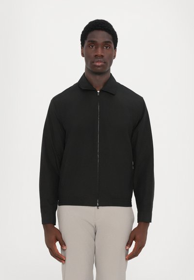 Sort lynlåsjakke med krave, lange ærmer og en glat tekstur. Har et minimalistisk design uden synlige mønstre eller accenter.