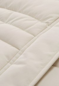 Edredón acolchado beige con costuras verticales, que presenta una textura suave y un borde ancho y doblado para un acabado pulido.
