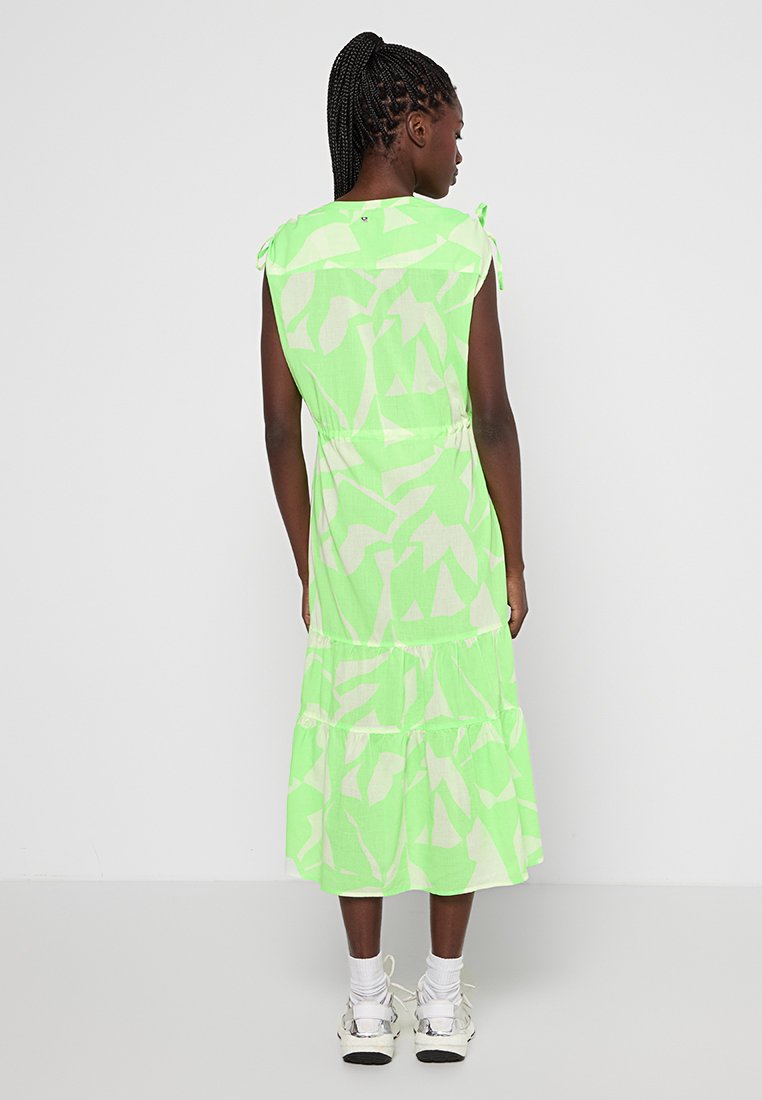 Zielona sukienka na ramiączkach w warstwy z abstrakcyjnym białym wzorem, luźny krój, szczegóły związane na ramionach. Wykonana z bawełny, lekka struktura.