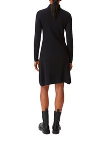 Robe en maille côtelée noire à manches longues et col montant, avec un ourlet évasé. Associée à des bottines noires.