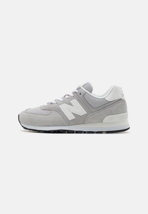 Šedá a bílá teniska New Balance s panely z broušené kůže a síťoviny, zavazování na tkaničky a gumová podrážka, zobrazena z bočního profilu na bílém pozadí.