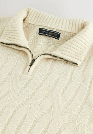 Krēma krāsas džemperis ar ribotu apkakli, ar priekšējo rāvējslēdzēju un kabelīšu adījuma tekstūru visā virsmā. Zīmola etikete novietota pie apkakles.