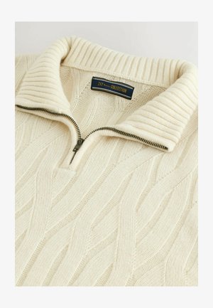 Krēma krāsas džemperis ar ribotu apkakli, ar priekšējo rāvējslēdzēju un kabelīšu adījuma tekstūru visā virsmā. Zīmola etikete novietota pie apkakles.