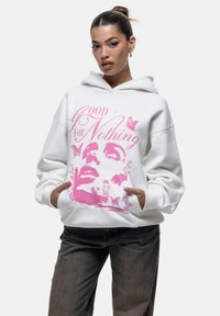 Witte hoodie met een roze grafisch ontwerp van een gezicht, bloemen en vlinders. Zachte stof met een relaxte pasvorm en een voorzak.