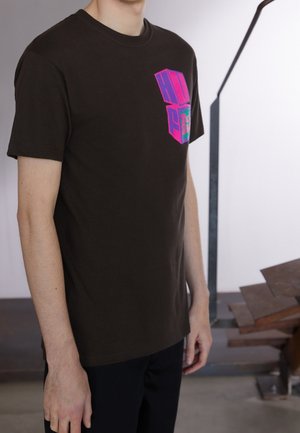 Brązowa bawełniana koszulka z krótkim rękawem, z kolorowym nadrukiem graficznym w neonowym różu i niebieskim na górnej lewej części przodu.