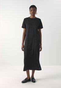 Rochie midi neagră, cu o croială lejeră, mâneci scurte și decolteu rotund. Material neted cu detalii subtile la cusături. Asociată cu încălțăminte neagră.