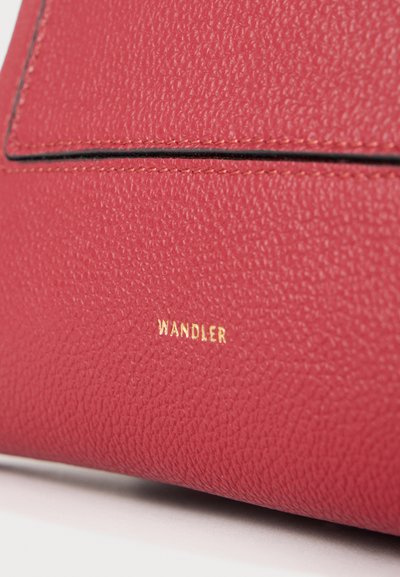 Gros plan sur un cuir rouge texturé avec une couture nette et le nom de marque Wandler embossé en or sur un sac à main.