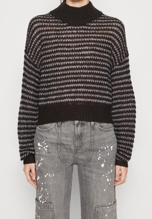 Sort og gråstribet strikket sweater med ribbet rullekrave og manchetter, kombineret med grå jeans med hvide malingstænk og lappelommer.