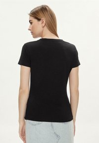 T-shirt nera aderente con maniche corte, scollo rotondo e una texture di cotone liscia. La vista posteriore mostra un design aderente e la semplicità.