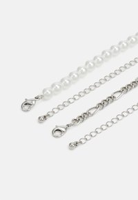 Tres cadenas de collar: una con perlas blancas, una cadena de eslabones de plata y una con varios acentos y cierres de plata.