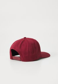 Red baseball cap with a solid fabric design, a curved visor, and an adjustable strap at the back featuring multiple sizing holes.